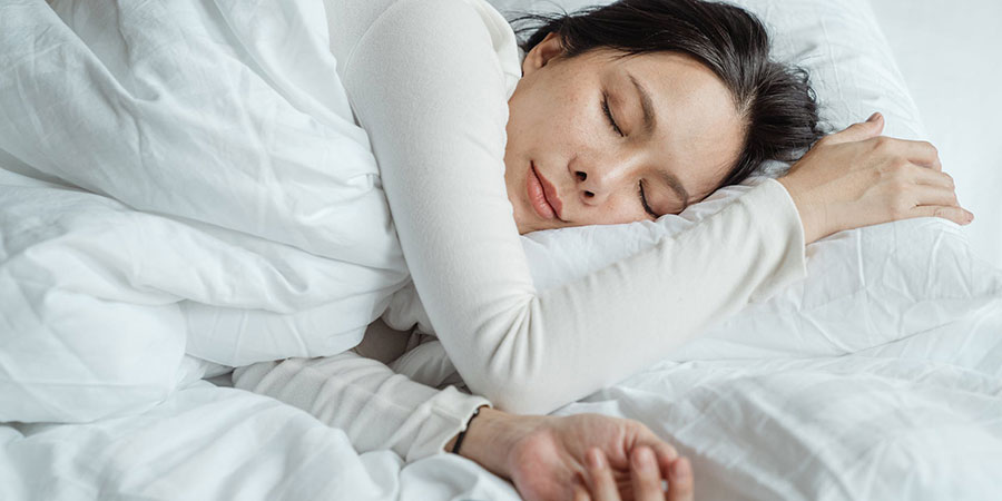 Asian woman with black straight hair sleeping on a bed with white bed sheets and white pillow